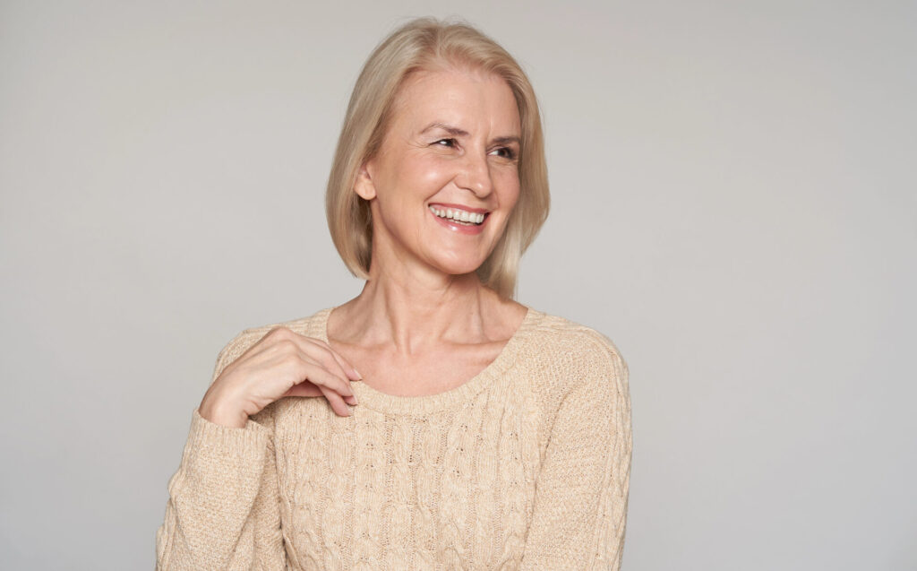 Starsza pani szeroko się uśmiecha, spoglądając w lewo