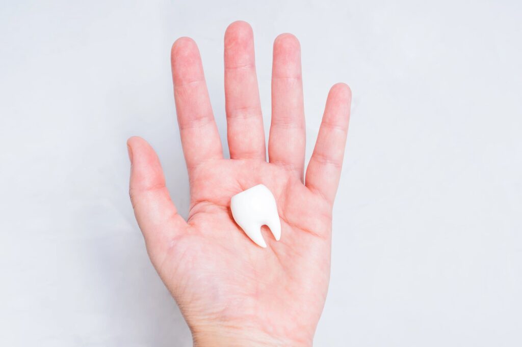 Męska dłoń, na której znajduje się duży sztuczny ząb