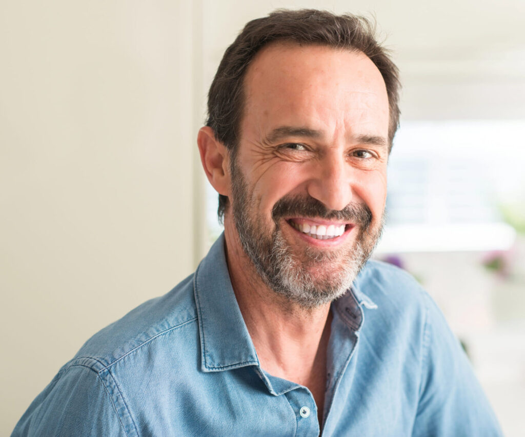 Mężczyzna w niebieskiej koszuli szeroko się uśmiecha, pokazując swoje zęby