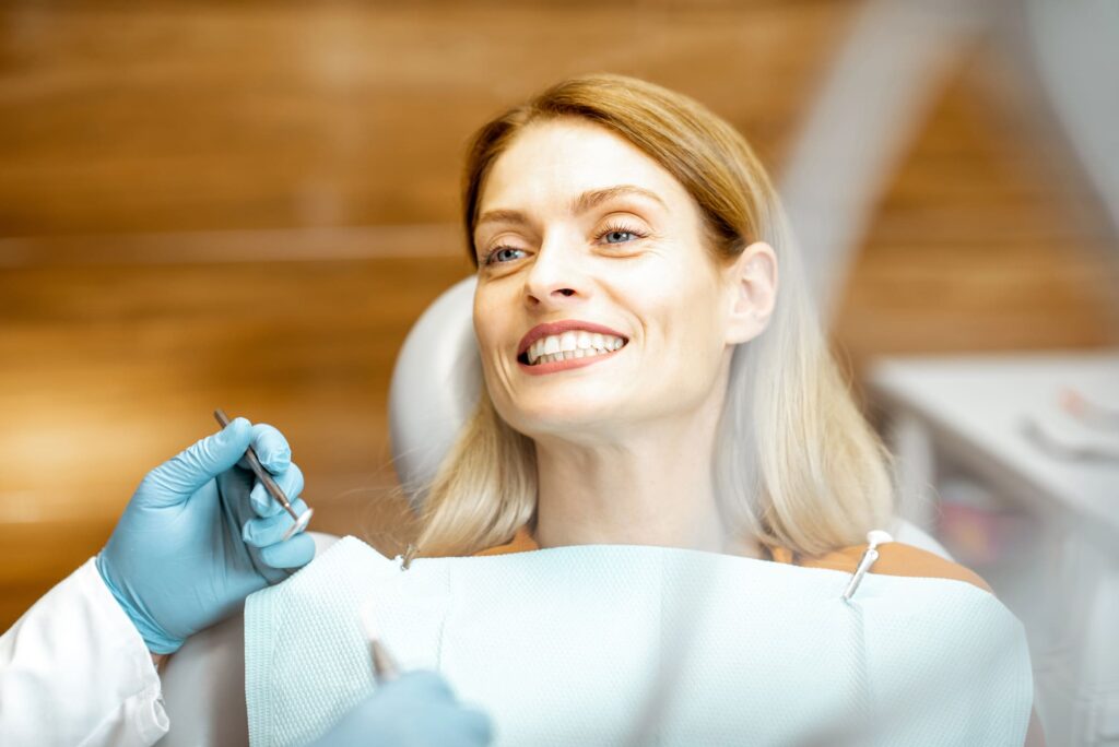 Kobieta siedzi na fotelu dentystycznym i szeroko się uśmiecha